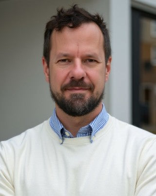 Man wearing a white sweater over a blue shirt with a blurred background
