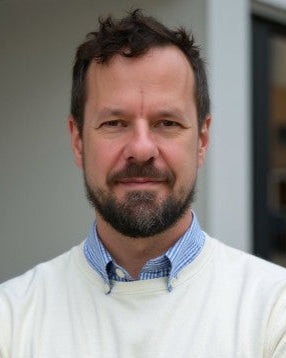 Man wearing a white sweater over a blue shirt with a blurred background